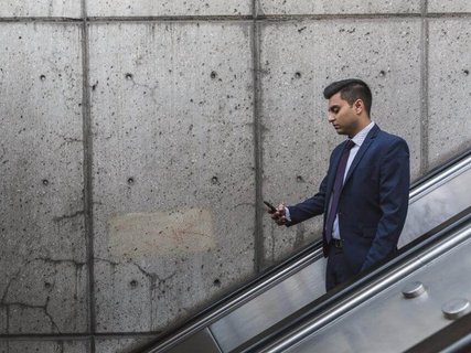 Ein Businessmann der auf einer Rolltreppe steht und währenddessen auf sein Handy starrt